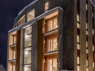 Experience modern living in this striking concrete and wood apartment building, illuminated against the night sky.