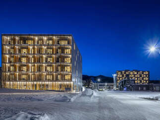 Experience modern living in this stunning multi-story building, featuring a unique facade with warm, illuminated interiors visible through expansive glass windows.