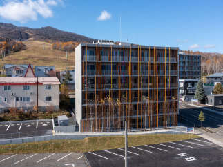 Discover modern living in this multi-story apartment building, featuring a striking facade with vertical wooden accents and numerous balconies offering scenic views.