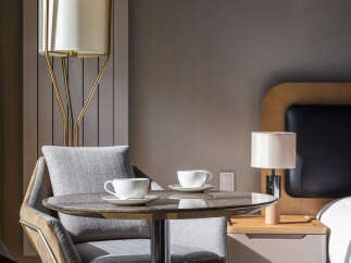 Experience comfort and style in this inviting hotel room, featuring a cozy seating area with two chairs and a marble-top table, perfect for enjoying morning coffee.