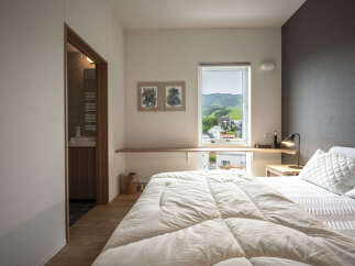 Experience serene living in this beautifully appointed bedroom, featuring a comfortable bed with plush white bedding and a stunning view of rolling green hills through a large window.