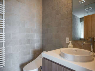 This modern bathroom features a sleek vanity with a white vessel sink and a chrome faucet, complemented by warm-toned brick-style tile walls.