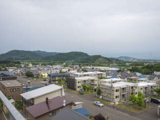 Discover this charming residential neighborhood with a mix of modern apartment buildings and traditional houses, nestled against a backdrop of lush green hills.