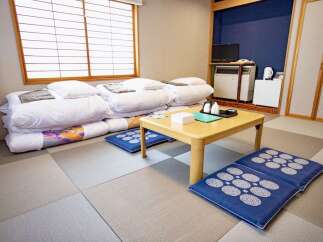 Experience traditional Japanese living with this serene room featuring comfortable futon bedding neatly stacked and ready for use.