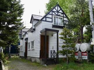 Charming white house with black trim and a distinctive Tudor-style gable, nestled amongst lush greenery.