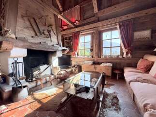 Experience rustic charm in this cozy mountain cabin living room, featuring a grand stone fireplace adorned with antique tools and a warm wooden interior.