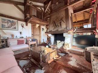 Experience rustic charm in this mountain retreat, featuring exposed wooden beams and a grand stone fireplace adorned with antique tools.