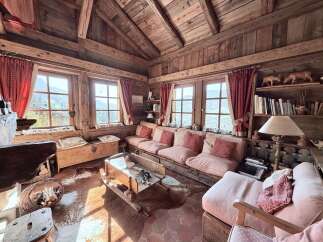 Experience rustic charm in this cozy mountain cabin living room, featuring exposed wooden beams and walls, a stone fireplace, and large windows offering stunning views.