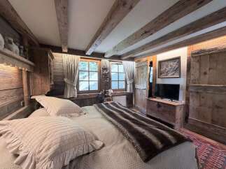 Experience rustic charm in this cozy bedroom, featuring exposed wooden beams and a plush bed adorned with ruffled pillows and a faux fur throw.