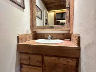 This rustic bathroom features a charming wooden vanity with a white sink and a large mirror, complemented by exposed wooden beams on the ceiling.