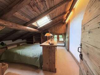 Experience rustic charm in this attic bedroom, featuring exposed wooden beams and a cozy sloped ceiling.