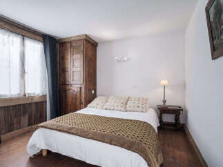 Experience rustic charm in this cozy bedroom, featuring a beautifully crafted wooden wardrobe and a comfortable bed adorned with patterned pillows.
