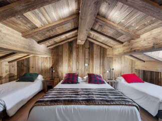 Experience rustic charm in this cozy attic bedroom, featuring exposed wooden beams and walls that evoke a warm, cabin-like atmosphere.