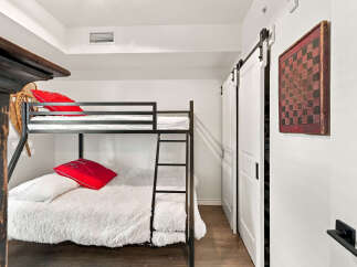 This bedroom features a space-saving bunk bed with plush white bedding and vibrant red accent pillows, perfect for accommodating guests or children.