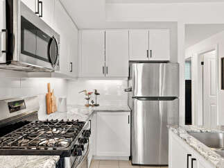 This modern kitchen features sleek stainless steel appliances, including a microwave, gas range, and refrigerator, complemented by white subway tile backsplash and granite countertops.