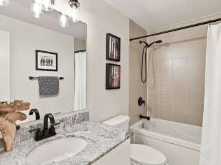 This modern bathroom features a sleek vanity with a granite countertop and a black faucet, complemented by a large mirror and decorative wall art.