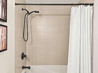 This modern bathroom features a sleek black showerhead and faucet set against a backdrop of elegant, neutral-toned square tiles.