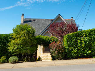 Charming home nestled behind lush green hedges and mature trees, offering privacy and a serene atmosphere.