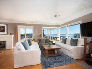 Experience breathtaking water and city views from this stunning living room, featuring a cozy fireplace and ample natural light.