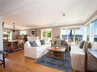 Experience breathtaking water and mountain views from this stunning living room, featuring comfortable slipcovered sofas and a rustic coffee table.