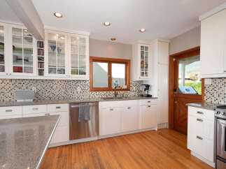 This spacious kitchen features pristine white cabinetry, including glass-front upper cabinets perfect for displaying dishware.