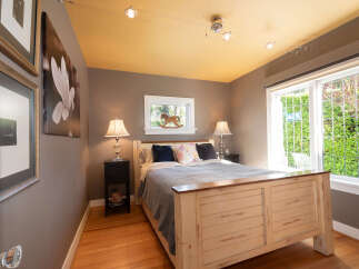 This charming bedroom features a comfortable queen-size bed with a distressed wooden frame, complemented by a cozy grey knit blanket and decorative pillows.