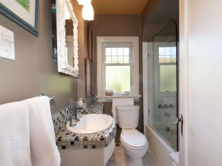 This charming bathroom features a stylish mosaic tile vanity surrounding a pristine white sink, complemented by a sleek chrome faucet.