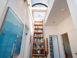 This hallway features a tall wooden bookshelf filled with books, illuminated by natural light from a large skylight.