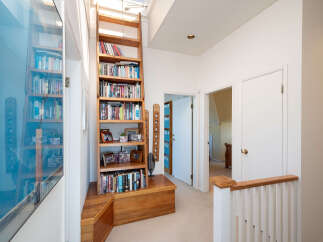 Discover a charming hallway featuring a tall wooden bookshelf filled with books and decorative items, complemented by a built-in wooden storage bench.