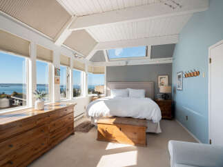 Wake up to breathtaking ocean views from this stunning bedroom, featuring a wall of windows and a skylight that flood the space with natural light.