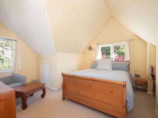 Discover this charming attic bedroom, bathed in soft yellow light and featuring a vaulted ceiling with white paneling.