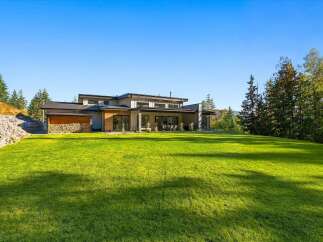 Experience modern luxury in this stunning home, featuring expansive green lawns and a backdrop of lush trees.