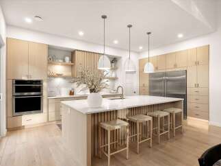 Experience modern luxury in this stunning kitchen, featuring sleek light wood cabinetry and a spacious island with vertical wood paneling.