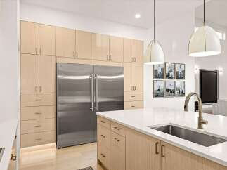 Experience modern luxury in this stunning kitchen, featuring sleek, light wood cabinetry that seamlessly integrates with a state-of-the-art stainless steel refrigerator.