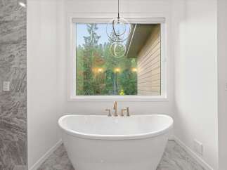 Indulge in relaxation in this luxurious bathroom, featuring a freestanding soaking tub positioned perfectly in front of a large window with serene forest views.