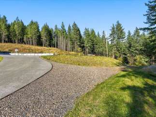 Discover the expansive grounds of this property, featuring a sweeping concrete driveway that curves gracefully through a landscape of lush green grass and natural gravel paths.
