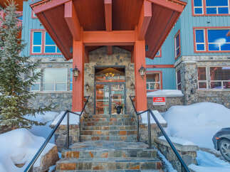 Experience the charm of this mountain lodge, featuring a welcoming stone entrance and a vibrant orange overhang, perfect for a cozy winter getaway.