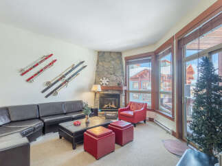Experience cozy mountain living in this inviting living room, featuring a striking stone fireplace and ample natural light from large windows.