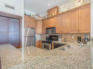 This spacious kitchen features beautiful light wood cabinetry, a sleek stainless steel refrigerator, and a granite countertop with a double sink.