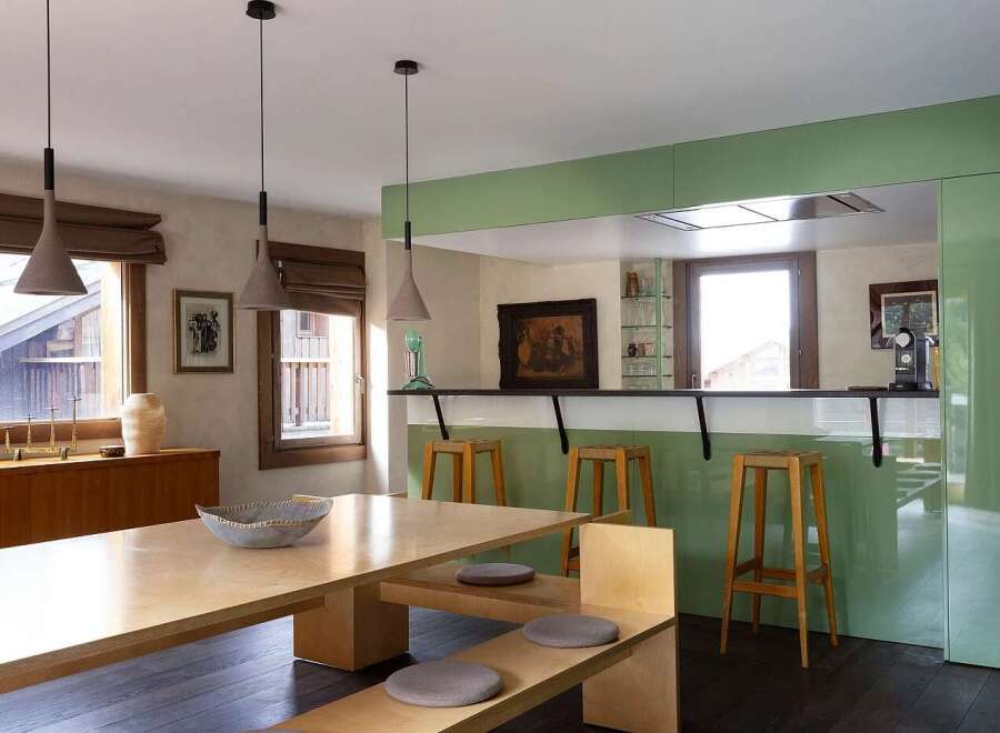This modern dining and kitchen area features a sleek, light wood dining table with a built-in bench, complemented by three cone-shaped pendant lights.