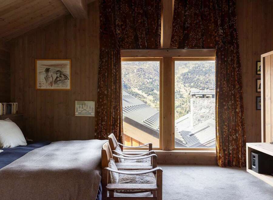 Experience breathtaking mountain views from this cozy bedroom, featuring warm wood paneling and large windows.