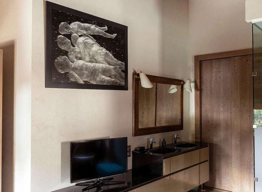 Experience luxury in this modern bedroom featuring a sleek double vanity with dual sinks and a large, framed artwork above a wall-mounted TV.