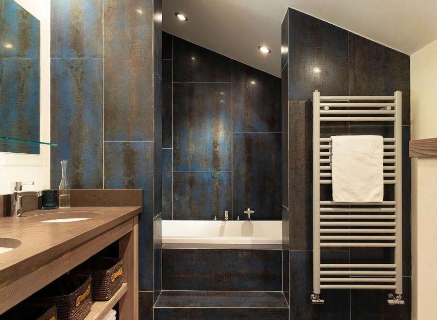 Experience modern luxury in this stunning bathroom featuring a deep soaking tub surrounded by striking blue and bronze metallic tiles.