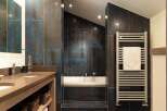 Experience modern luxury in this stunning bathroom featuring a deep soaking tub surrounded by striking blue and bronze metallic tiles.