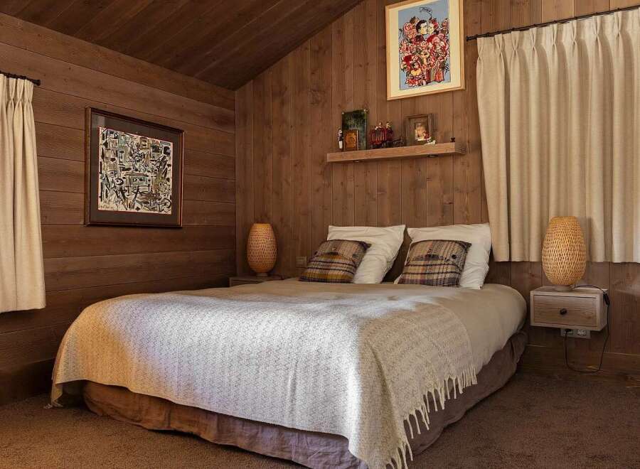 Experience cozy cabin living in this charming bedroom, featuring warm wood-paneled walls and a comfortable bed adorned with plush pillows and a textured throw.