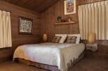 Experience cozy cabin living in this charming bedroom, featuring warm wood-paneled walls and a comfortable bed adorned with plush pillows and a textured throw.