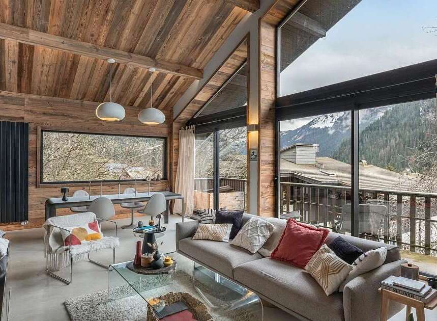 Experience luxurious mountain living in this stunning chalet, featuring a vaulted wood-beamed ceiling and expansive windows that frame breathtaking alpine views.