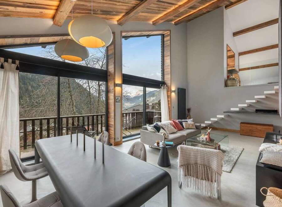Experience breathtaking mountain views from this stunning living space, featuring a soaring vaulted ceiling with exposed wooden beams and a wall of windows.