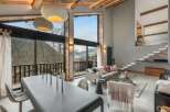 Experience breathtaking mountain views from this stunning living space, featuring a soaring vaulted ceiling with exposed wooden beams and a wall of windows.