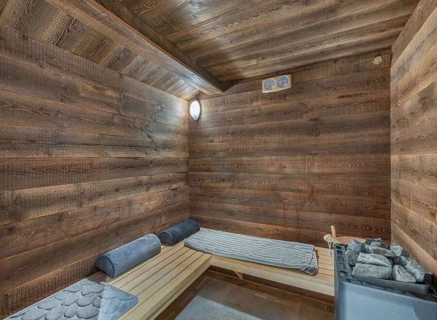 Experience ultimate relaxation in this luxurious wooden sauna, featuring a modern electric heater and a stack of hot stones.